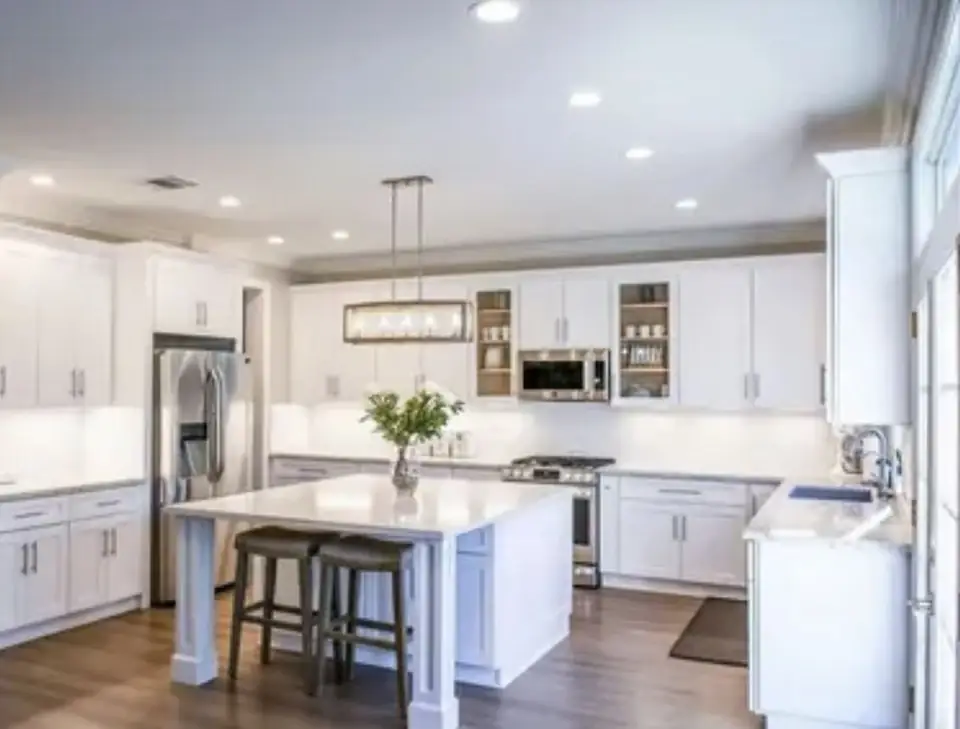 Bright white shaker-style kitchen with a quartz island and brass linear pendant
